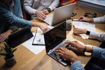 Close up cropped top angle view of multi ethnic company workers sitting late at office and using modern gadgets. Men and women analysing financial report during meeting.