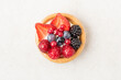 Freshly backed tartlet with strawberries, blueberries, raspberries on beige stone background. Top view, flat lay of food photography minimal concept
