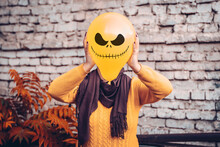 Girl In Yard Holding Inflatable Balloon With An Evil Face In Her Hands Outside Happy Halloween Concept Holiday Card Street Style Autumn Season Costume Jack-o-lantern For Carnival