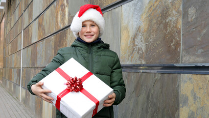 Close-up shot of Happy adorable boy in Santa Claus hat with her Christmas present. Winter holidays	