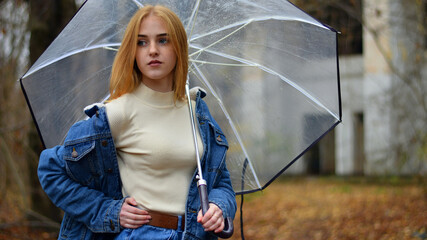 young girl with umbrella walking in at beautifu autumn park. modern girl in casual clothes walks through the city park. Seasonal style, autumn beauty. autumn season, in a blue jacket, in autumn leaves