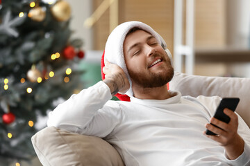 Young man in headphones with mobile phone at home on Christmas eve