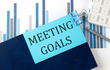 Poster - MEETING GOALS on sticky note on notebook on the chart background