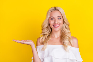 Sticker - Portrait of attractive cheerful wavy-haired girl holding on palm copy blank space ad isolated over bright yellow color background