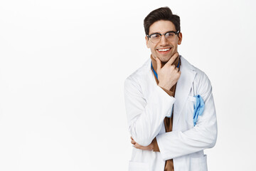 Wall Mural - Smiling physician in medical robe, looking thoughtful and pleased, thinking of smth, standing over white background