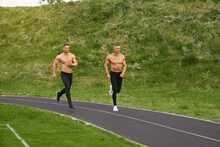 Handsome Muscular Guys With Naked Torso Spending Free Time For Running On Fresh Air. Active Exercises Of Two Bodybuilders. Sport Activity On Stadium.