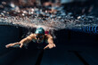 Underwater view of swimming movements details. One female swimmer in swimming cap and goggles training at pool, indoors.