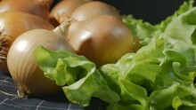 Close-up, Rotation, Juicy Green Salad Leaves And Golden Onions On A Dark Checkered Fabric