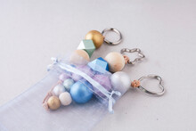 Painted Wooden Beads Key Chains In Organza Gift Bag On Light Background. Wooden Beads And Hexagon In Pink, Green, Blue And Gold Metallic Colors. Crafts Concept...