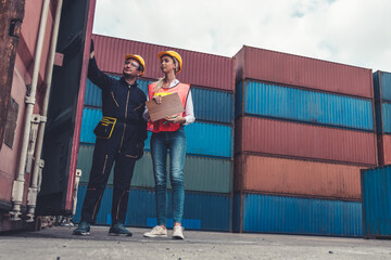 Industrial worker works with co-worker at overseas shipping container yard . Logistics supply chain management and international goods export concept .