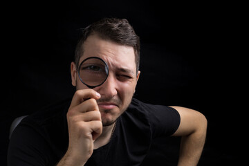 Young handsome man and a magnifying glass on black background in low key. Search symbol. Investigation concept