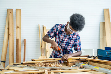 Portrait of african american little child wearing shirt standing with a drill in hands and help dad assembling furniture shelf with power screwdriver tool, learning concept.