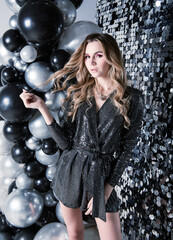 1 white young attractive blonde woman with long hair in a black sequined dress on a silver  shiny ball background