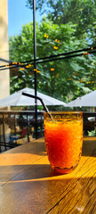 Wall Mural - Vertical selective focus of orange juice in a glass cup on a wooden table at an outdoor cafe