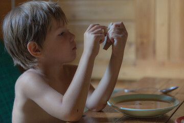 Portrait of small boy child eating soup meal or breakfast having lunch by the table at home with spoon white