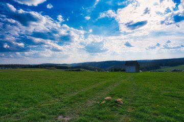 Canvas Print - Small house in a meadow field on a cloudy sky background.