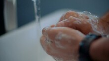 Caucasian man washing and disinfecting his hands in slow motion then rinsing them while waring a sports watch and ring.