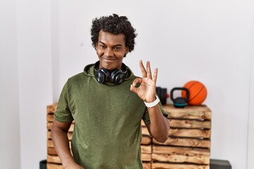 Poster - African man with curly hair wearing sportswear at the gym smiling positive doing ok sign with hand and fingers. successful expression.