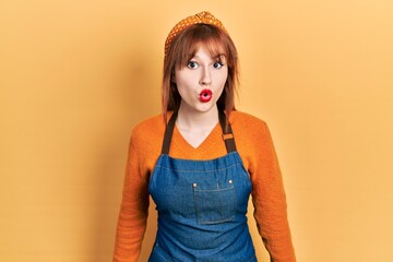 Canvas Print - Redhead young woman wearing apron scared and amazed with open mouth for surprise, disbelief face