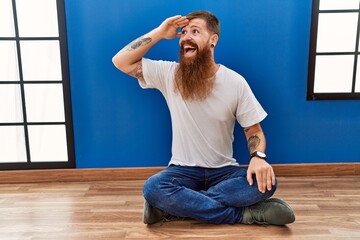 Sticker - Redhead man with long beard sitting on the floor at empty room very happy and smiling looking far away with hand over head. searching concept.