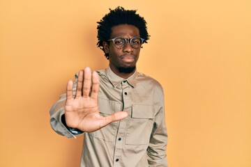 Sticker - Young african american man wearing casual clothes and glasses doing stop sing with palm of the hand. warning expression with negative and serious gesture on the face.