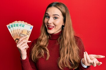 Sticker - Young blonde woman holding euro banknotes celebrating achievement with happy smile and winner expression with raised hand