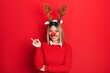 Beautiful hispanic woman wearing deer christmas hat and red nose with a big smile on face, pointing with hand and finger to the side looking at the camera.