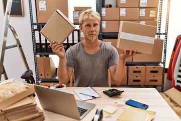 Sticker - Young blond man holding packages working at online shop relaxed with serious expression on face. simple and natural looking at the camera.