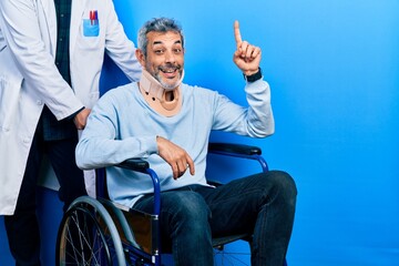 Canvas Print - Handsome middle age man with grey hair on wheelchair wearing cervical collar pointing finger up with successful idea. exited and happy. number one.