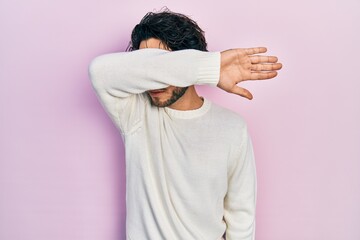 Sticker - Handsome hispanic man wearing casual white sweater covering eyes with arm, looking serious and sad. sightless, hiding and rejection concept