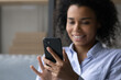 © fizkes - Close up focus on smartphone in smiling African American woman hand, happy young female looking at phone screen, chatting online in social network, typing message, surfing internet or shopping