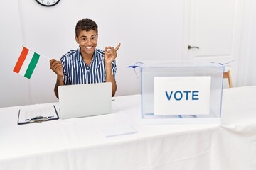 Poster - Young handsome hispanic man at political campaign election holding hungary flag smiling happy pointing with hand and finger to the side