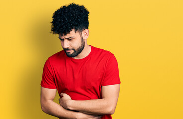 Young arab man with beard wearing casual red t shirt with hand on stomach because indigestion, painful illness feeling unwell. ache concept.