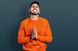 © Krakenimages.com - Young hispanic man with beard wearing casual orange sweater begging and praying with hands together with hope expression on face very emotional and worried. begging.