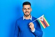 Young hispanic man with beard holding zimbabwe flag looking positive and happy standing and smiling with a confident smile showing teeth
