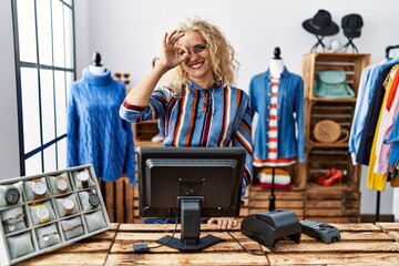 Wall Mural - Middle age blonde woman working as manager at retail boutique doing ok gesture with hand smiling, eye looking through fingers with happy face.