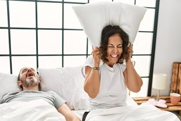 Sticker - Middle age hispanic man snoring and woman angry covering ears with pillow at bedroom.