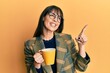 © Krakenimages.com - Young hispanic woman wearing business style drinking cup of coffee smiling happy pointing with hand and finger to the side