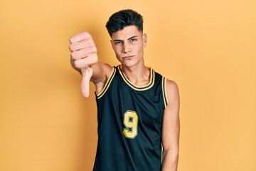 Wall Mural - Young hispanic man wearing basketball uniform looking unhappy and angry showing rejection and negative with thumbs down gesture. bad expression.