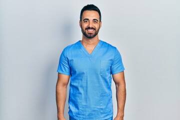 Handsome hispanic man with beard wearing blue male nurse uniform with a happy and cool smile on face. lucky person.