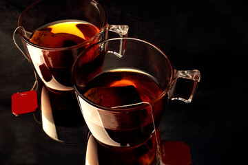 two cups of hot tea in a glass cup with reflection on a dark background