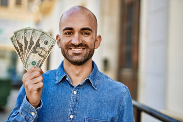 Poster - Young hispanic man smiling happy holding dollars at the city.