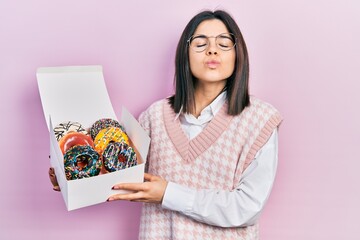 Canvas Print - Young brunette woman holding tasty colorful doughnuts looking at the camera blowing a kiss being lovely and sexy. love expression.