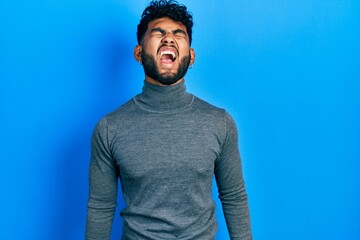 Wall Mural - Arab man with beard wearing turtleneck sweater angry and mad screaming frustrated and furious, shouting with anger. rage and aggressive concept.