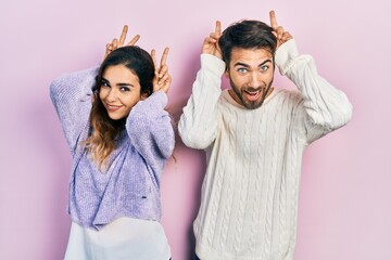 Young hispanic couple wearing casual clothes posing funny and crazy with fingers on head as bunny ears, smiling cheerful