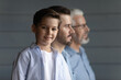 Three generations. Intergenerational family of 3 diverse age men older hoary grandfather young handsome father little junior school age boy son grandson stand in row. Focus on child looking at camera