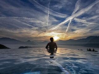 Back of young Asian man without shirt standing in the modern swimming pool admired calm beautiful seascapes surrounded by mountains with amazing cloud appeared as a line in the blue sky during sunset