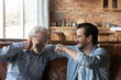 © fizkes - Give me five dad. Laughing old father bumping fists with adult son sitting on sofa at home having fun talking joking relaxing on weekend. Happy aged dad support grown kid encourage greet with success