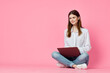 © VICHIZH - cheerful woman with laptop sitting on the floor on a pink background