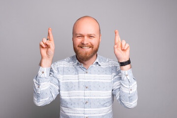 Cheerful and smiling young bearded man in casual crossing fingers and dreaming